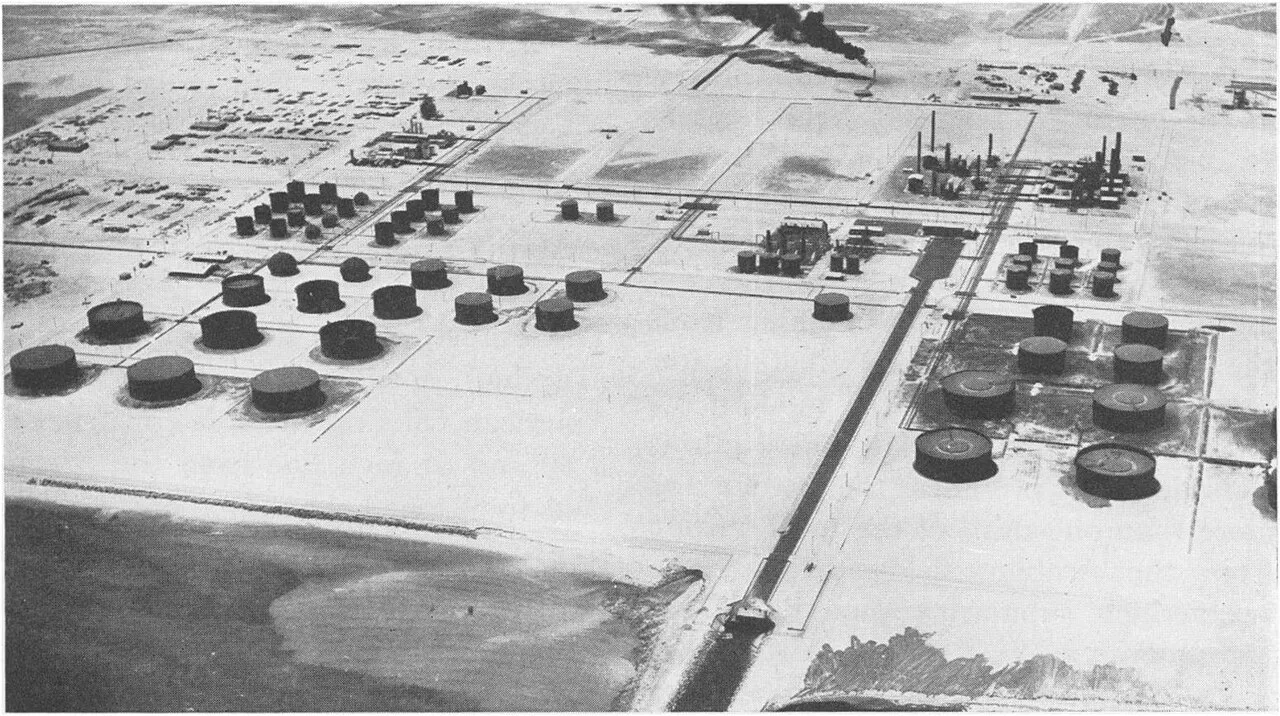 An archival aerial photograph of Aramco's Ras Tanura refinery and tank farm on the Gulf coast, near Dhahran (file photo). Ras Tanura is Aramco's principal export terminal; this historical photograph does not depict the Dhahran headquarters or any event reported in this article.