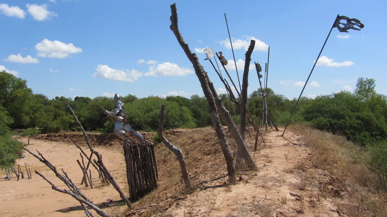 The memorial sculpture at Fortín Boquerón in the Paraguayan Chaco — a metal soldier figure on a timber post amid dry scrub and old positions under a wide sky. Modern photograph of the memorial site, not a depiction of the 1932 battle.