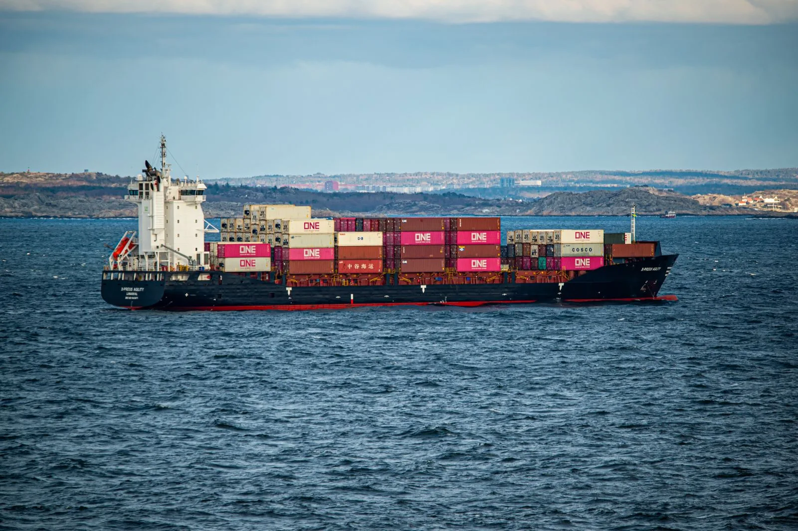 A container ship underway near a coastline.